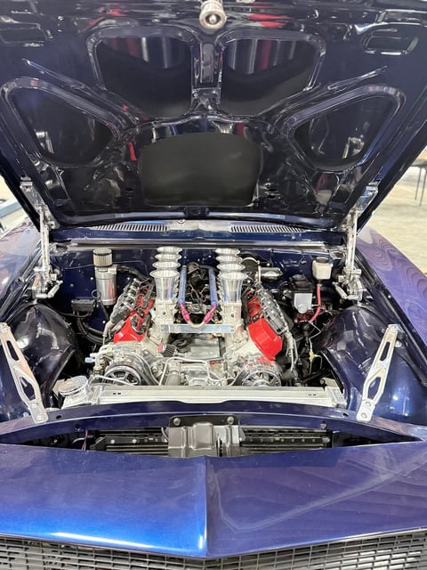 Open hood of classic blue car revealing chrome and red engine with detailed mechanical components