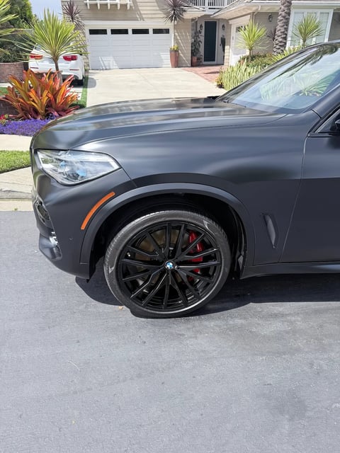 Gray BMW SUV with black alloy wheels parked on residential street with palm trees and house in background