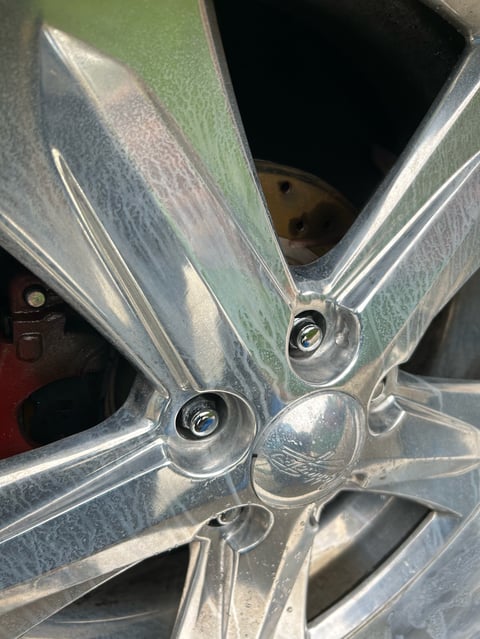 Close-up of a silver alloy wheel hub with lug nuts and visible brake components through the center opening