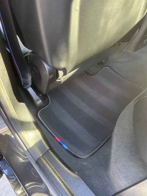 Black car floor mats with white stitching on rear passenger seat area of vehicle interior