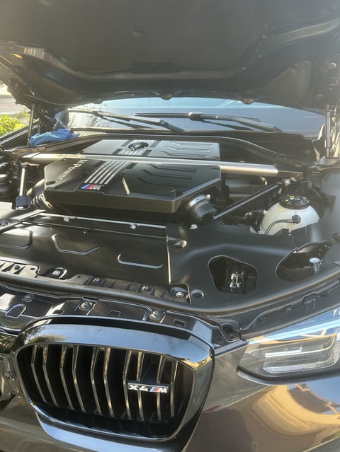 Open engine compartment of a BMW X4 showing V8 engine with chrome accents and black grille visible at bottom