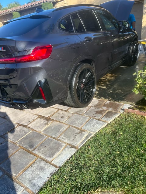 Black luxury SUV parked on a driveway with stone pavers and lawn, view of rear and side profile