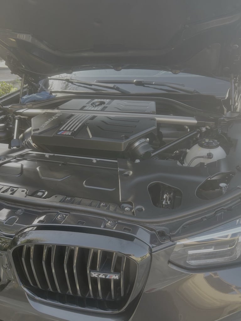 Open car engine compartment showing motor and mechanical components under bright daylight