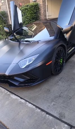 Black Lamborghini sports car with open scissor doors parked on a residential driveway