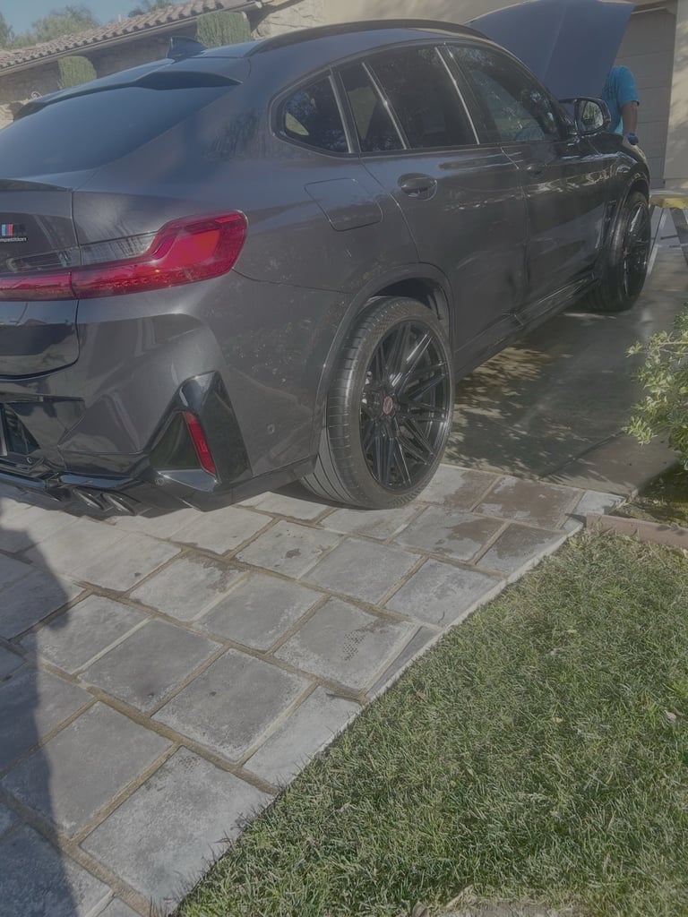 Dark gray BMW SUV parked in driveway with open hood, paved pathway and grass visible