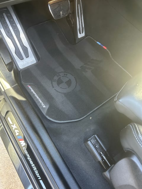 Black custom car floor mat with BMW logo and white stitching inside vehicle interior