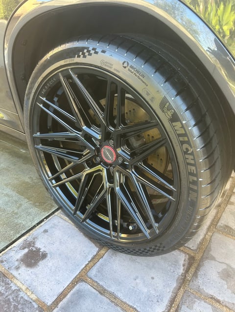 Close-up of a black multi-spoke alloy wheel with a red center cap on a parked vehicle, showing the tire and wheel rim detail